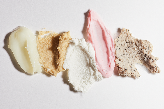 Dažādi ādas kopšanas līdzekļi, krēmi, skrubji izsmērēti uz balta fona.